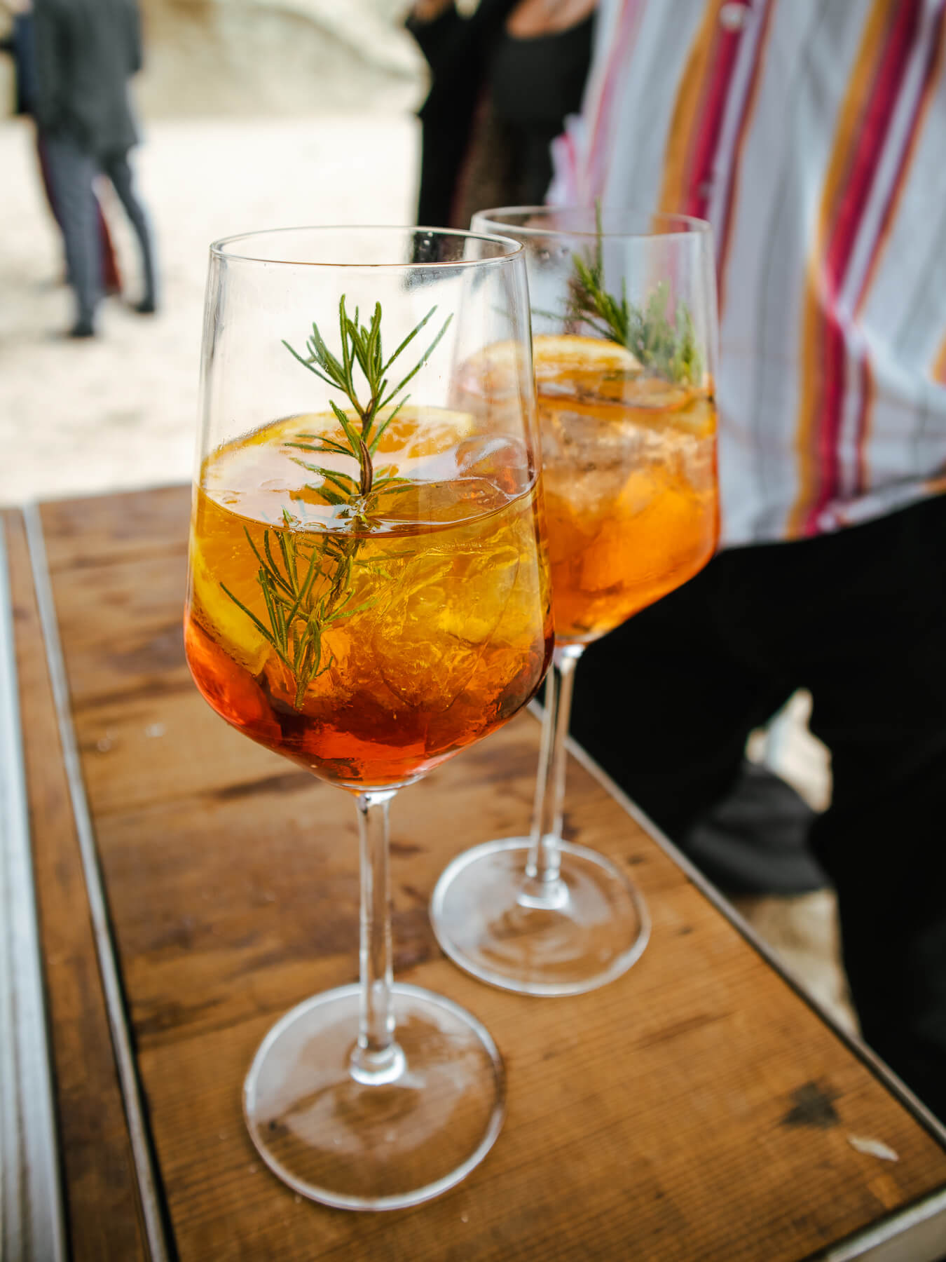 Two cocktail with rosemarry garnish and oranges in wine glass